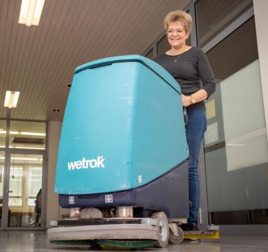 Hausabwartin mit blauem Putzwagen im Gang